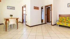 A spacious living area with a dining table and chairs, a colorful sofa, and a hallway leading to another room.