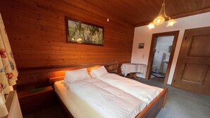 Une chambre à coucher avec une tête de lit en bois, un lit recouvert de draps blancs, un tableau au-dessus du lit et une porte en bois.