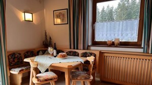 Un coin repas chaleureux avec une table et des bancs en bois, une fenêtre donnant sur les arbres et un radiateur.