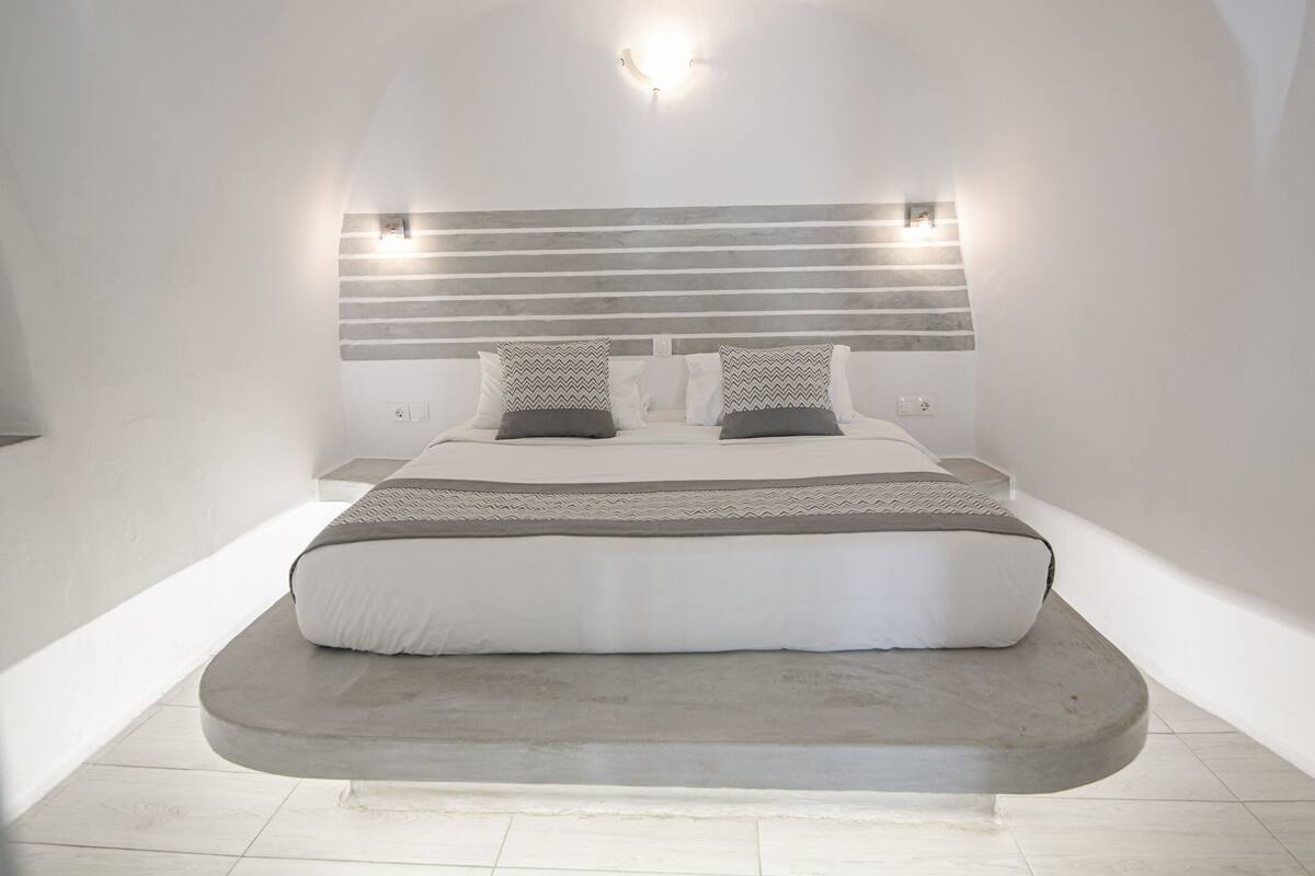 Ein modernes Schlafzimmer mit einem bogenförmigen Bett, einem Kopfteil mit integrierter Beleuchtung und einer neutralen Farbgestaltung.