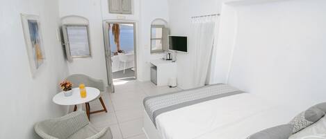A white room with a bed, a desk, a chair, and a small table with a plant and a glass of orange juice.