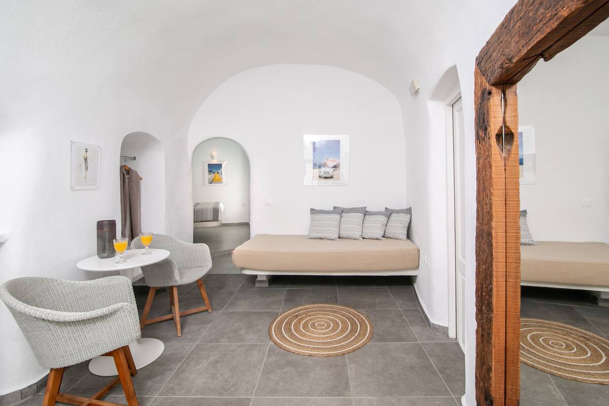 Ein modernes, minimalistisches Zimmer mit einer Couch, zwei Sesseln, einem kleinen Tisch mit Getränken und einem Teppich.