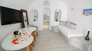 Una sala de estar moderna con un sofá blanco, una mesa de comedor con una botella y copas, y un televisor montado en la pared.