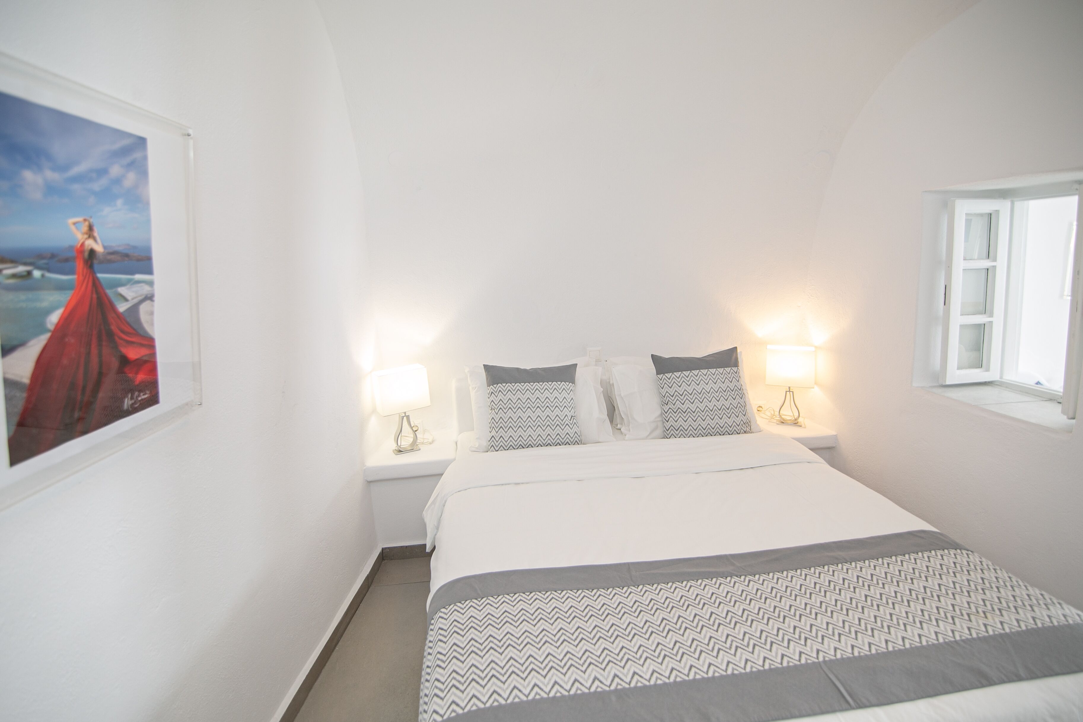 A bedroom with a bed, two bedside lamps, a window, and a wall-mounted picture.