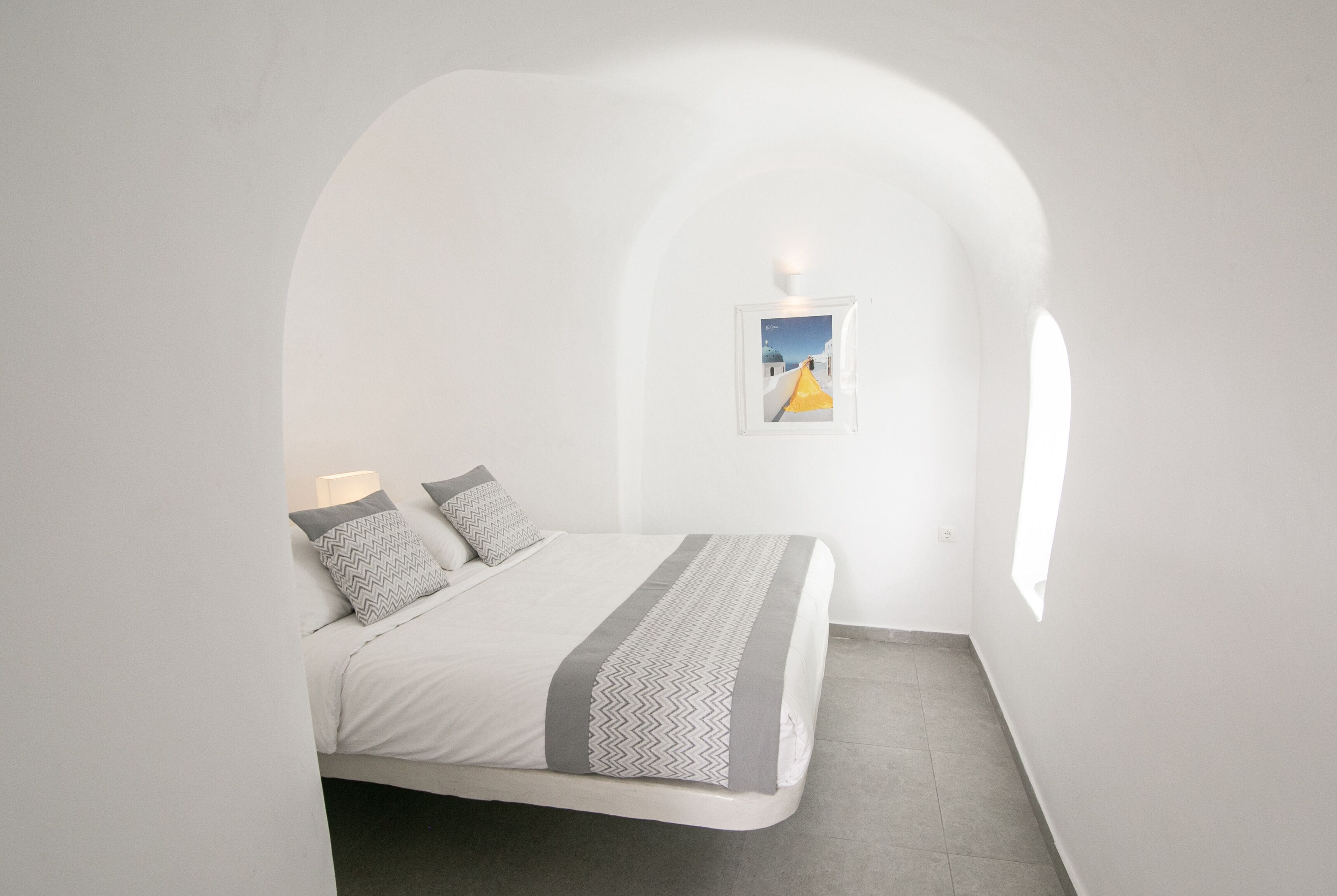Ein Schlafzimmer mit Bett, Kissen, einem Nachttisch, einem gerahmten Bild und einem Fenster.