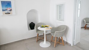 Una habitación moderna y minimalista con pared blanca, una mesa redonda, dos sillas de mimbre, un pequeño jarrón negro y un cuadro enmarcado.