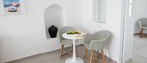 A modern, minimalist room with a white wall, a round table, two wicker chairs, a small black vase, and a framed picture.