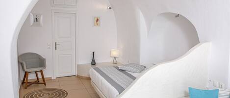 Une chambre à coucher avec un lit, une chaise, une table de chevet, une lampe et une porte.
