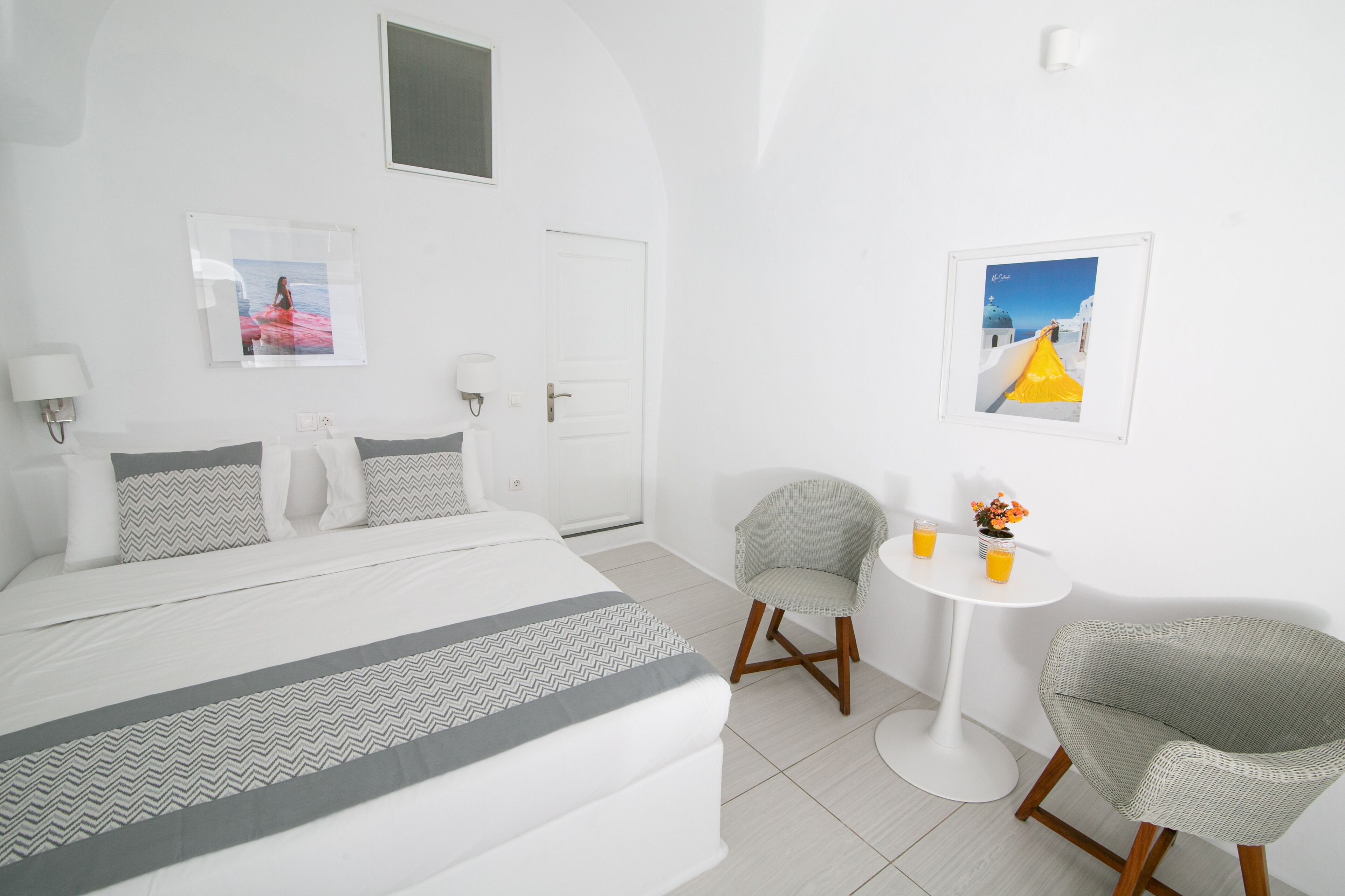 A hotel room with a bed, two chairs, a small table with drinks, and two framed pictures on the wall.