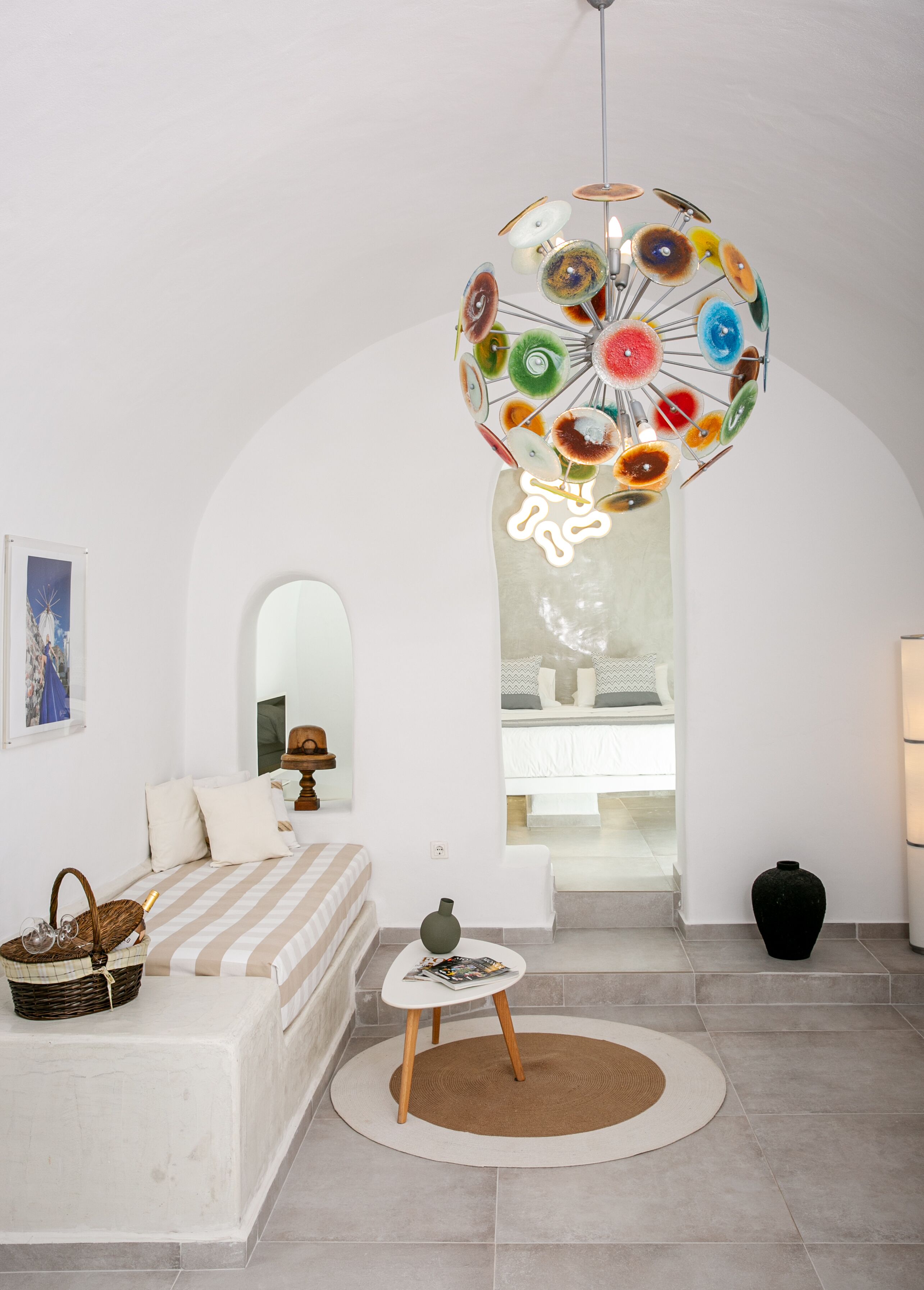 A modern living room with a unique spherical chandelier, a white sofa, a small side table, and a view of a bedroom through an arched doorway.