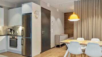 Une cuisine moderne dotée d’un four et d’un réfrigérateur encastrés, un coin repas avec une table et des chaises en bois, et une grande fenêtre avec des rideaux.