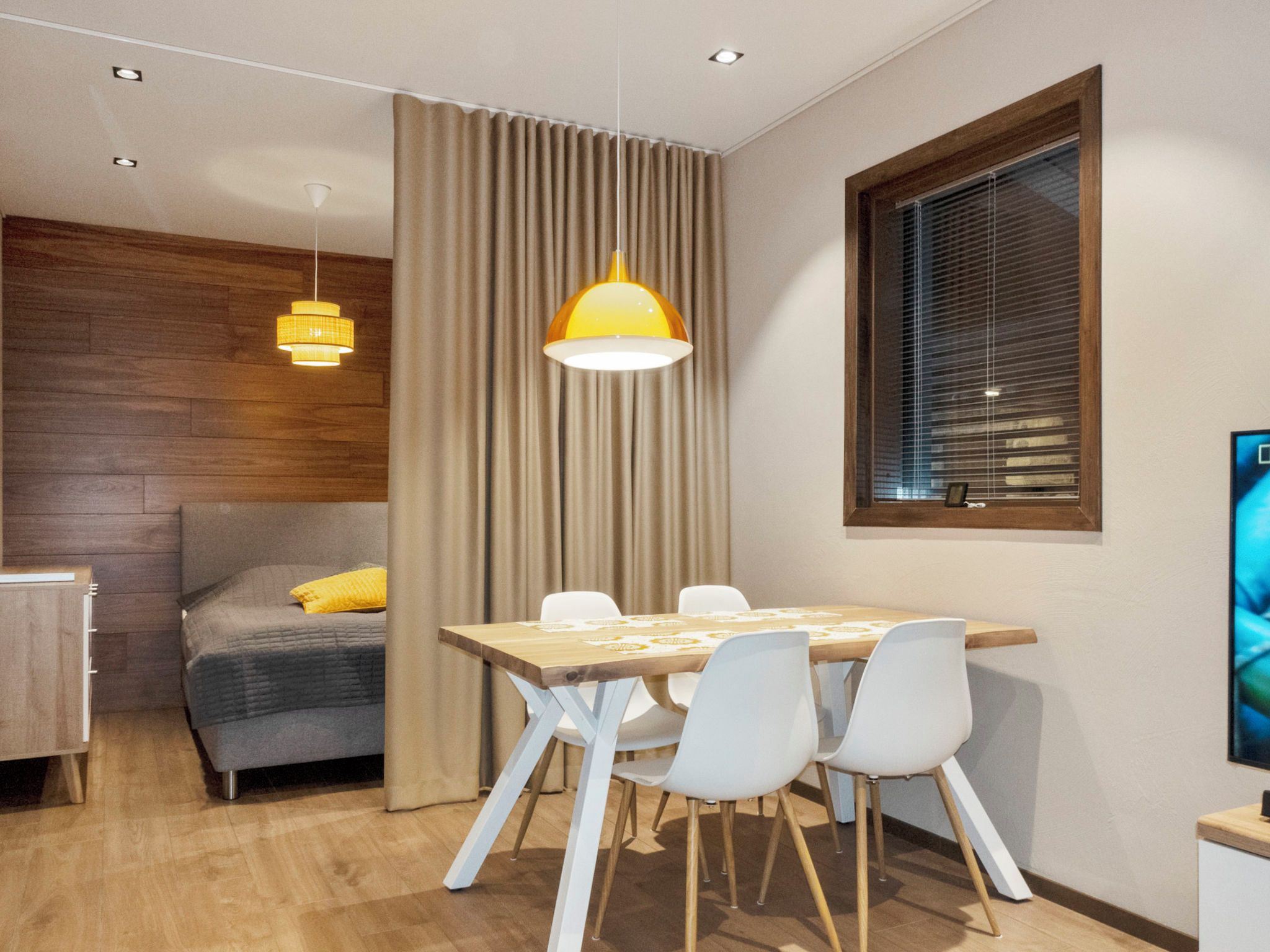A modern room with a dining table, chairs, a sofa, and a window with blinds.
