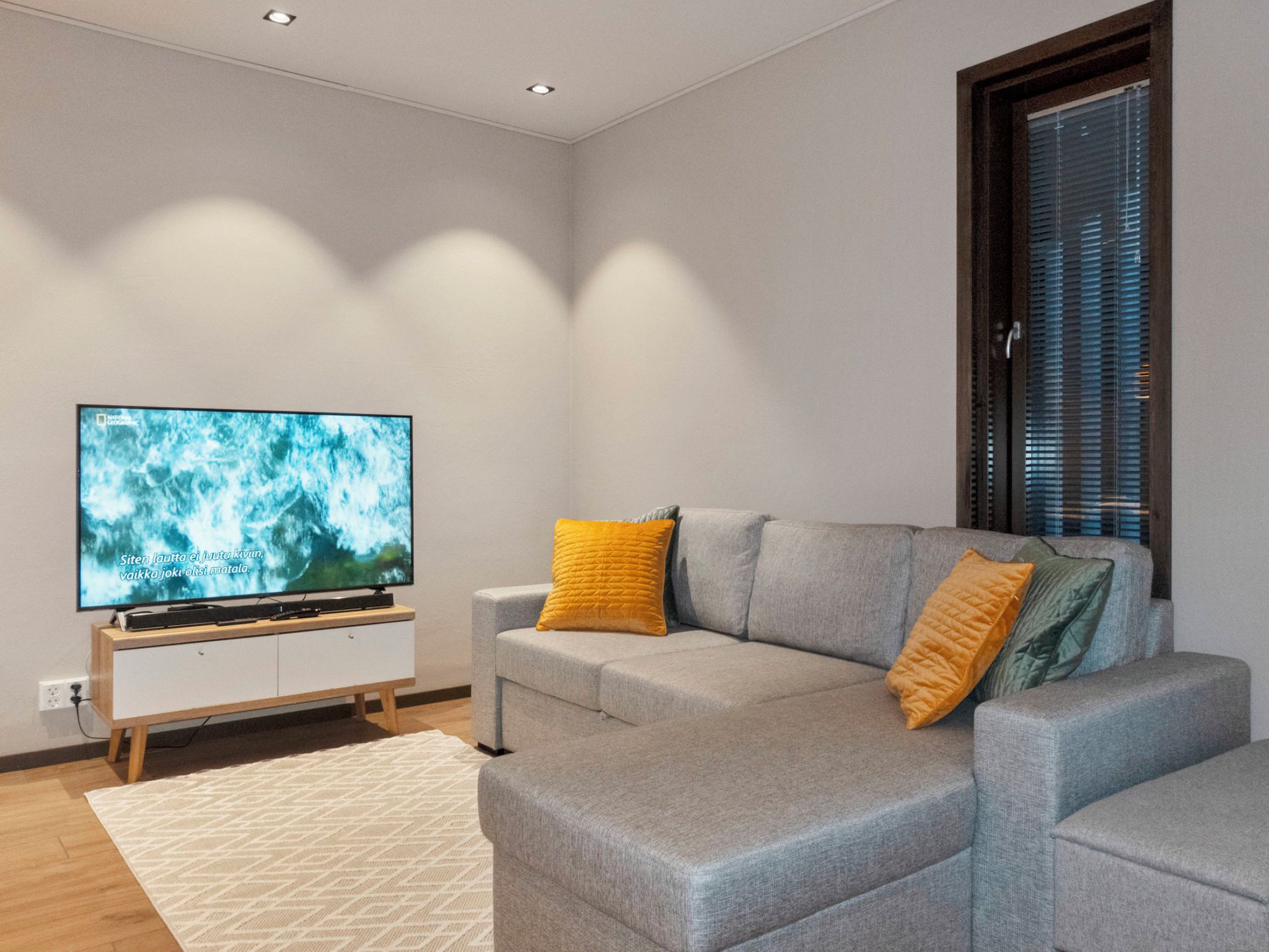 A modern living room with a grey sofa, a flat-screen TV, and a wooden cabinet.