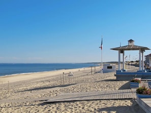 A beach with a gazebo, a flagpole, and a wooden boardwalk.