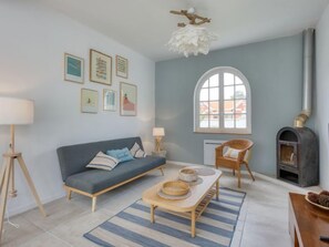 Una sala de estar con un sofá, una mesa con cuencos, una silla, una chimenea y cuadros en la pared.