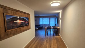 Un corridoio con pavimento in legno, un tavolo da pranzo con sedie, un divano e un quadro appeso al muro.