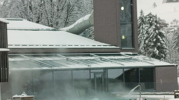 Un edificio con area piscina vetrata, circondata da alberi innevati e facciata in mattoni.
