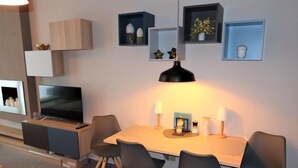 Un salon moderne avec un téléviseur, une table à manger avec des chaises et des étagères décoratives.