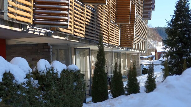 Un bâtiment moderne doté d’une façade en bois et surplombant un paysage enneigé.