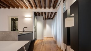 A modern kitchen with wooden beams, a dining area with a table and chairs, and a hallway with a mirror and curtains. - Sant'Angelo Apartment by Wonderful Italy (Venice)