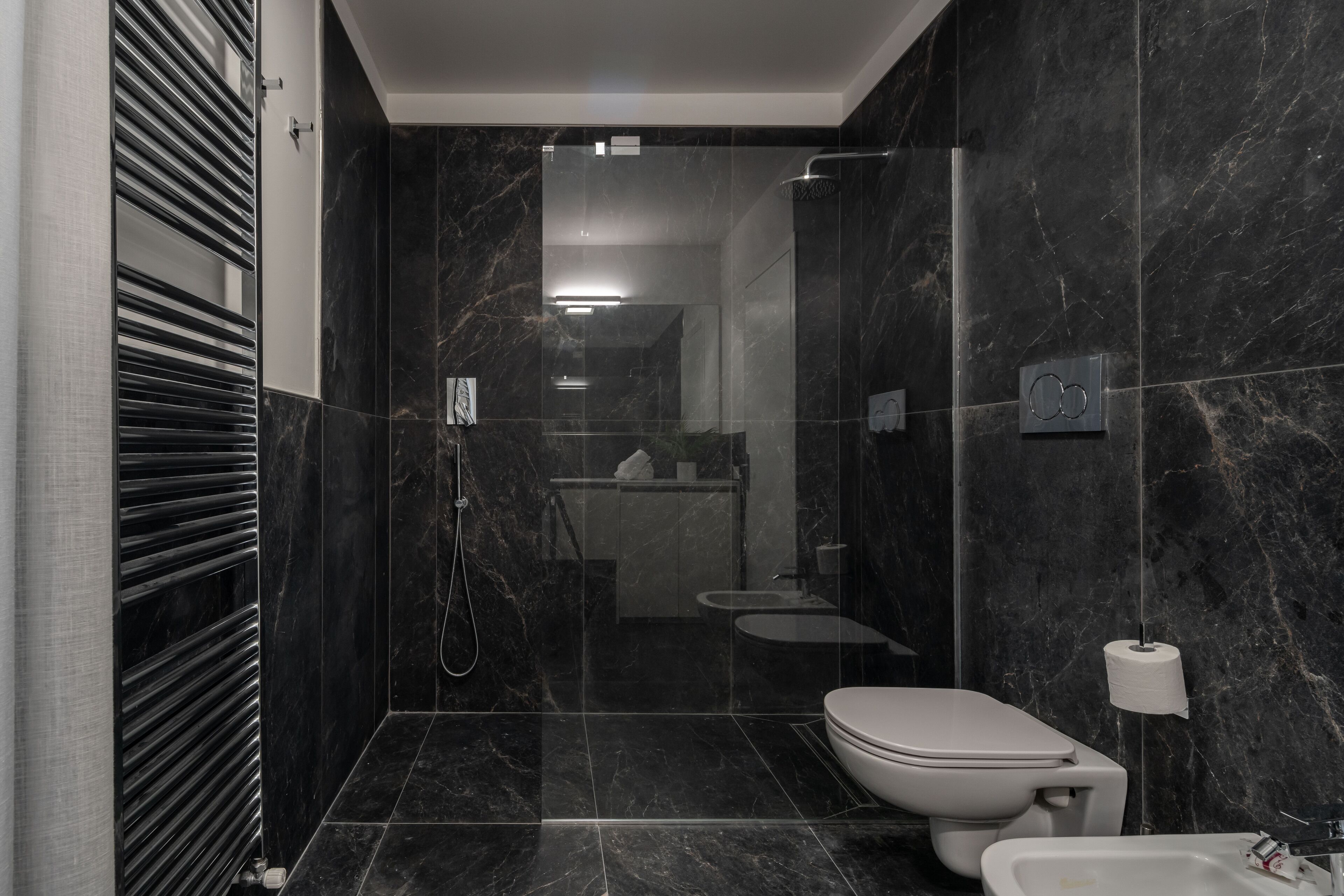 A modern bathroom with a toilet, bidet, and shower area, featuring dark marble walls and a sleek design.