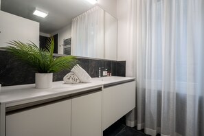 A modern bathroom with a white vanity, a potted plant, a towel, and a mirror.