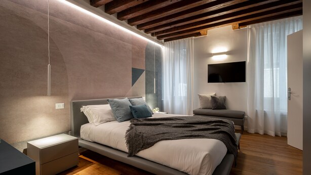 A modern bedroom with a bed, bedside tables, a TV, and a window with curtains. - Sant'Angelo Apartment by Wonderful Italy (Venice)