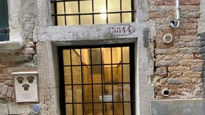 A building entrance with a metal gate, a number plaque, and a small window with a grid pattern. - Sant'Angelo Apartment by Wonderful Italy (Venice)