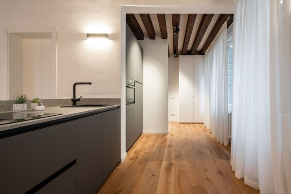 A modern kitchen with a wooden floor, a built-in island, and a large window with sheer curtains.