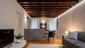 A modern living room with a wooden ceiling, a grey sofa, a flat-screen TV, and a dining area with a table and chairs. - Sant'Angelo Apartment by Wonderful Italy (Venice)