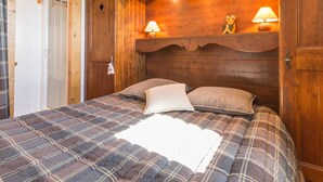Una camera da letto con copriletto a quadri, due cuscini, una testiera in legno con motivo a festoni e due lampade da comodino.