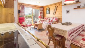 Una stanza accogliente con arredamento in legno, un tavolo da pranzo illuminato da una lampada rossa e vista panoramica attraverso un'ampia vetrata scorrevole.