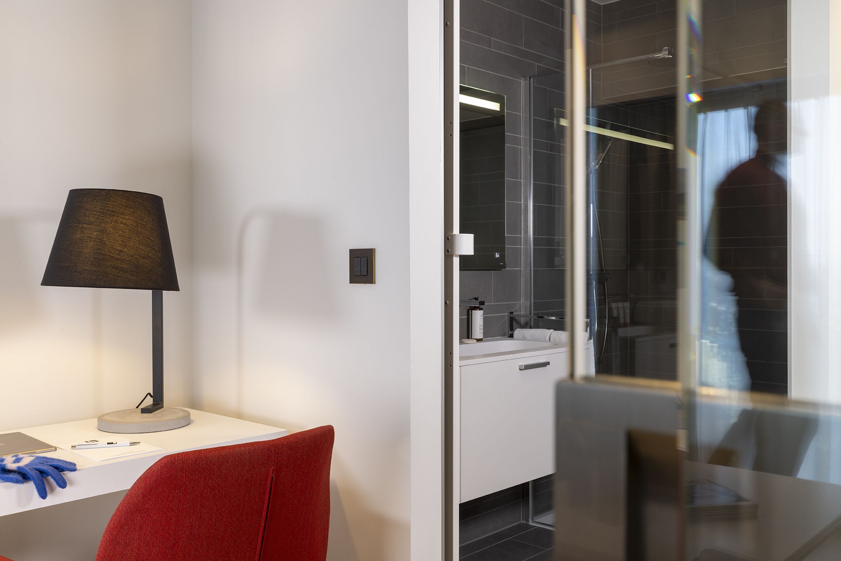 A modern hotel room with a desk, chair, and a glass shower enclosure.