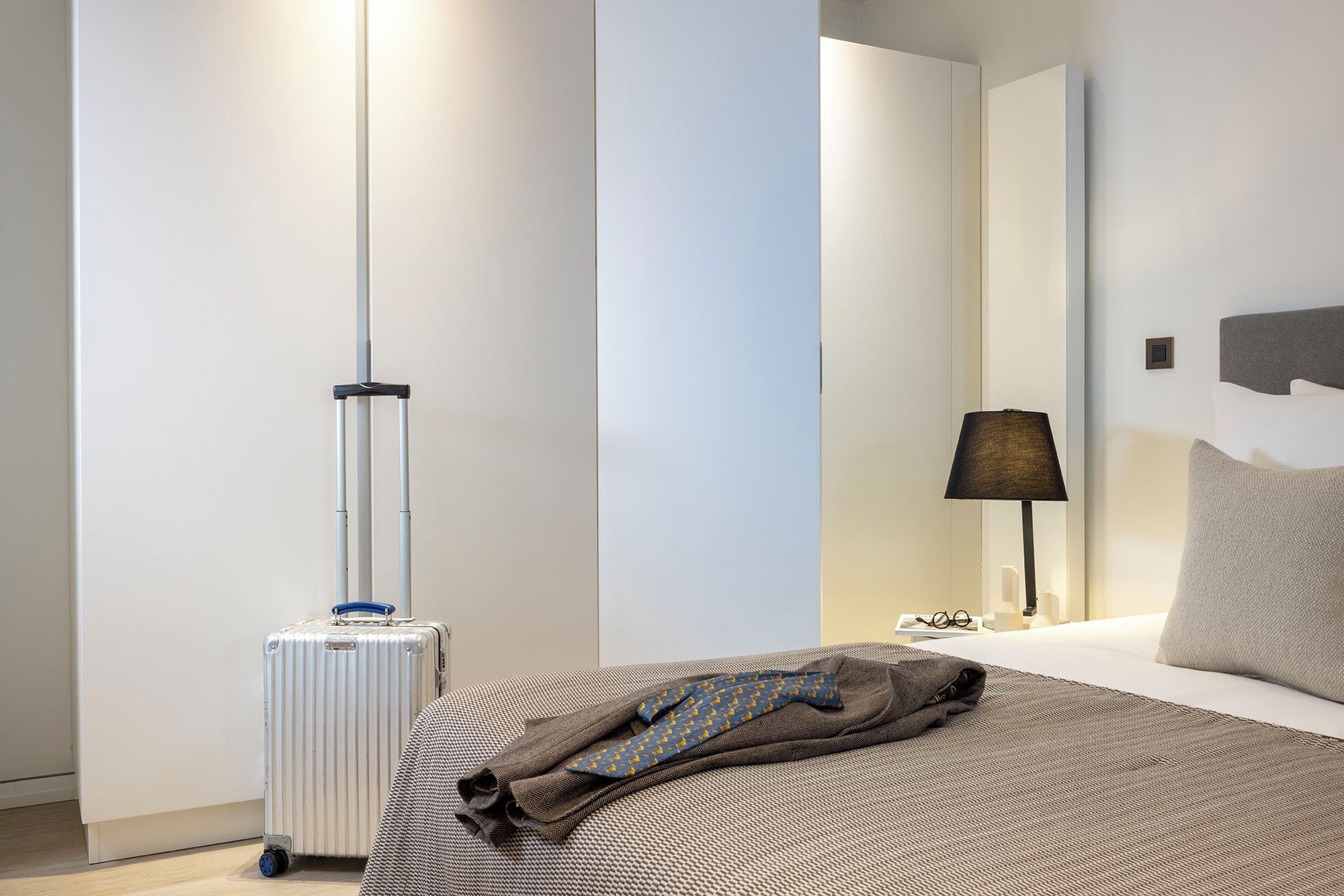 Une chambre d’hôtel avec un lit, une valise, une lampe et une table de chevet.