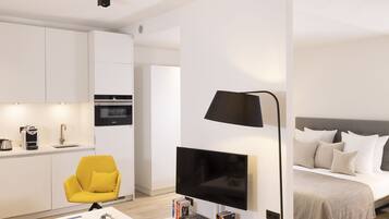 A modern hotel room with a flat-screen TV, a sofa, a bed, and a kitchenette.