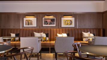 A modern hotel lobby with a seating area, a dining table, and artwork on the wall.