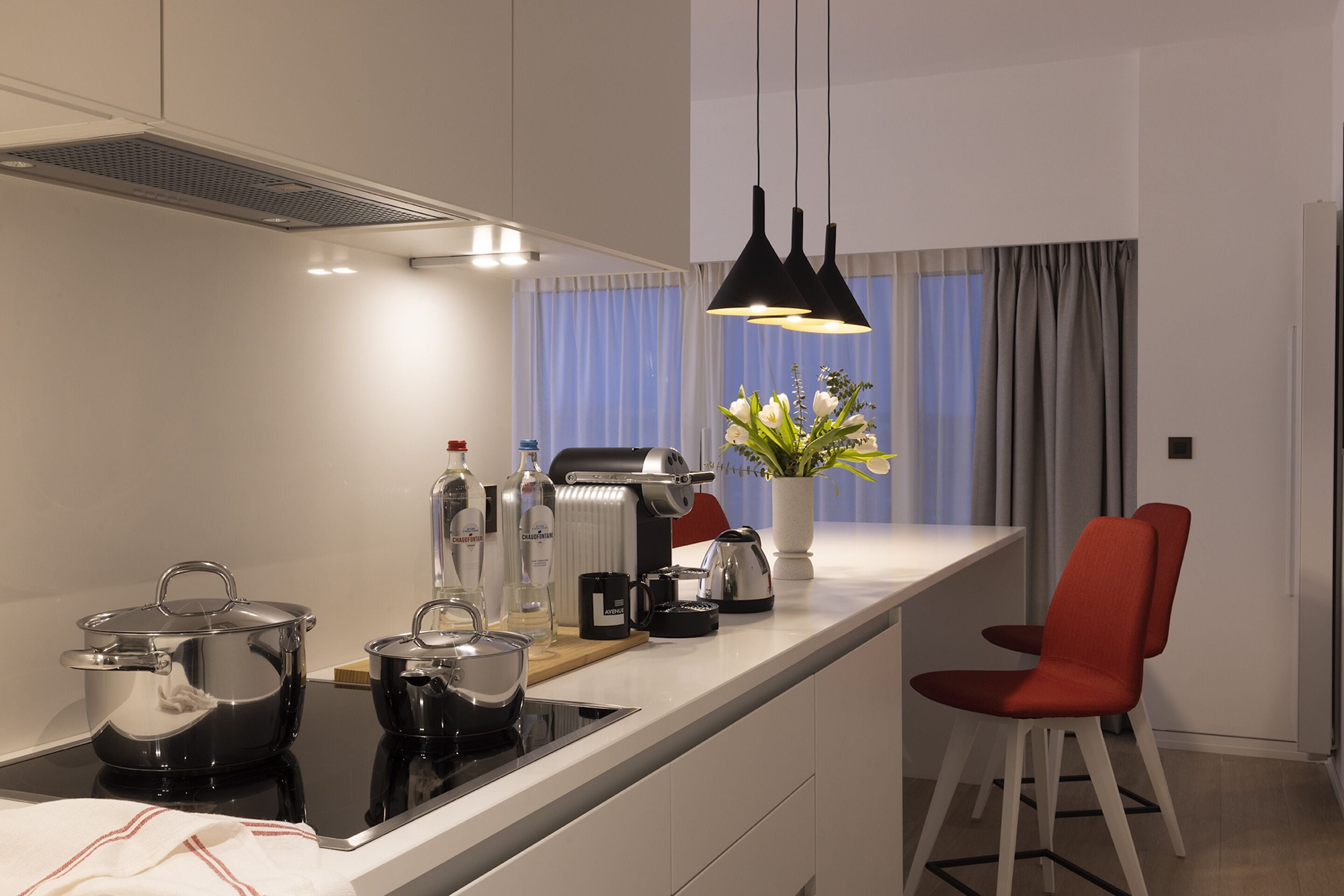 A modern kitchen with a central island, a coffee machine, and a red chair.