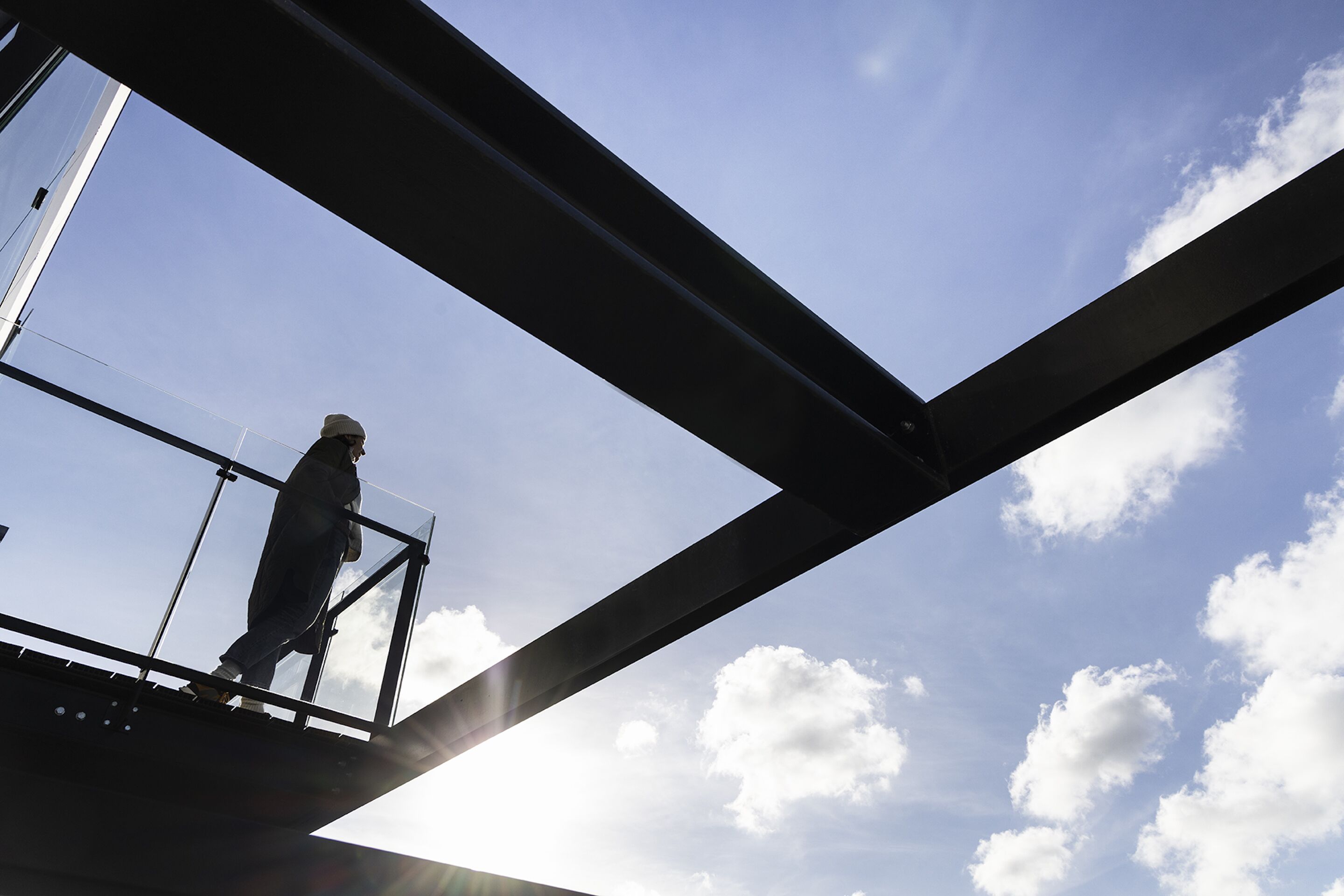 A person standing on a balcony with a clear sky and clouds in the background.