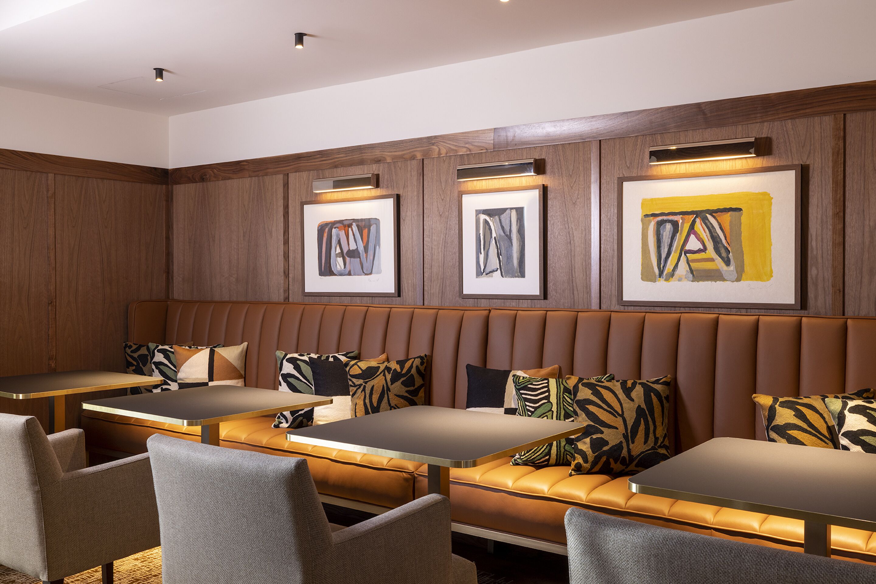 A modern lounge area with leather booths and tables, framed artwork on the walls, and a wooden panel design.