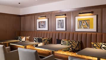 A modern lounge area with leather booths and tables, framed artwork on the walls, and a wooden panel design.