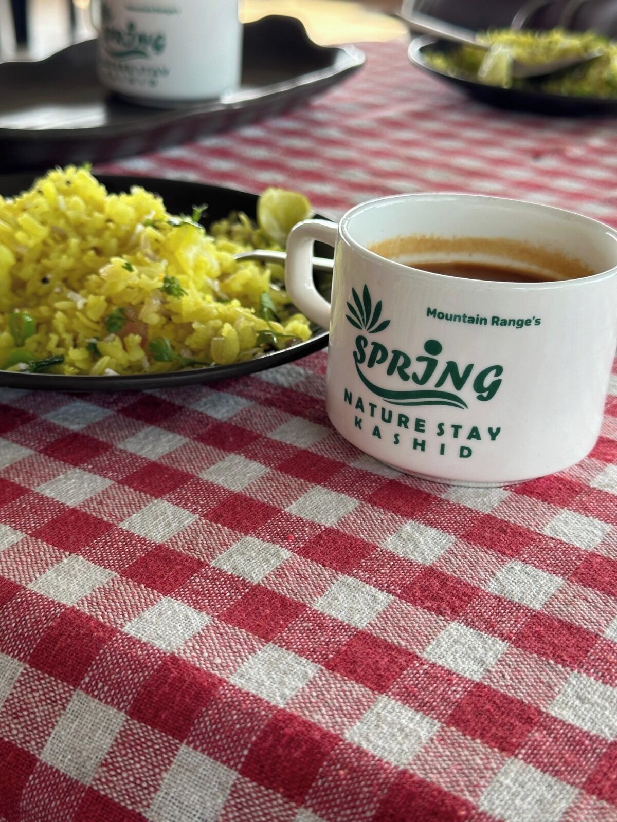Een tafel met een geruit tafelkleed, een witte mok met tekst, en een bord gele rijst.
