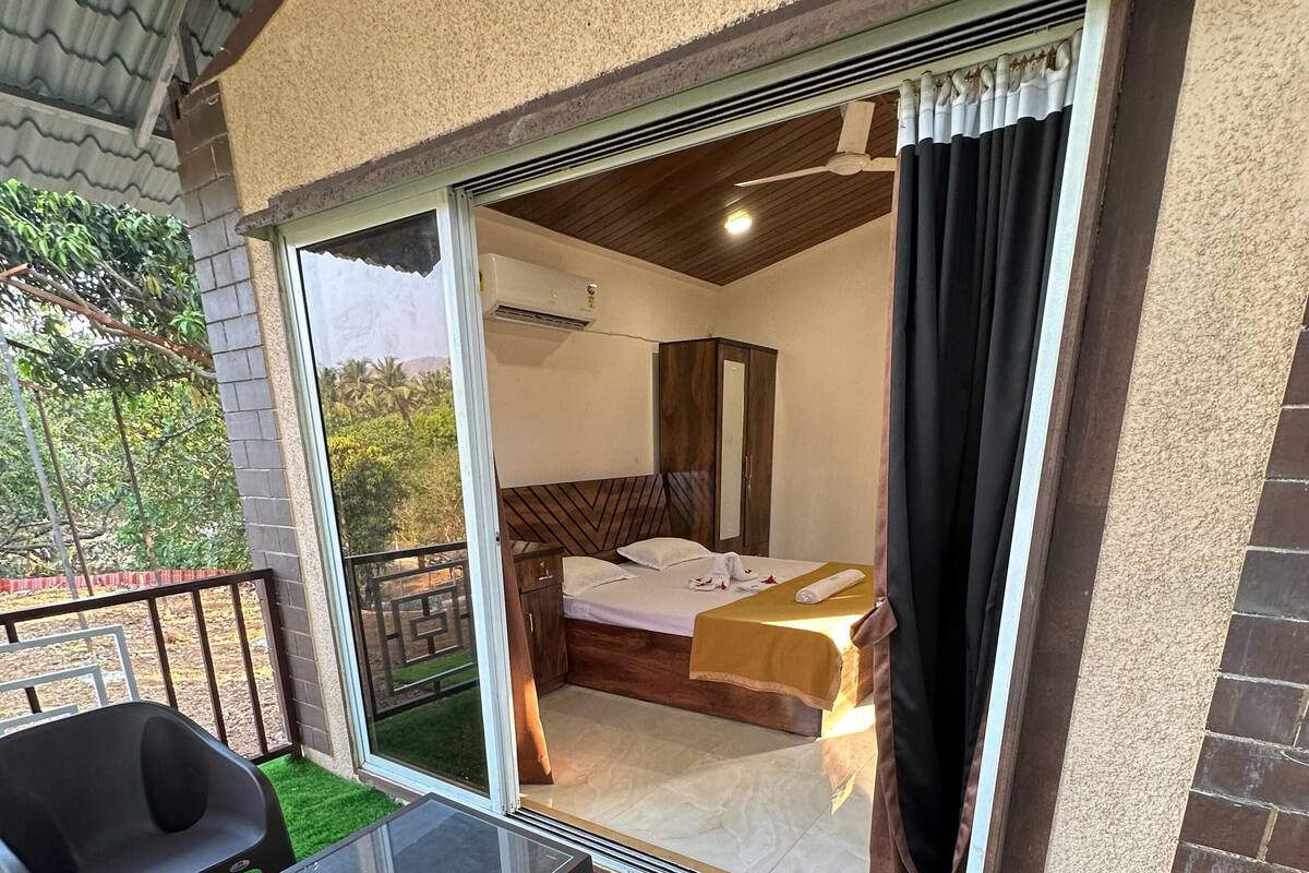A room with a bed, a wardrobe, and a sliding glass door leading to a balcony with artificial grass.