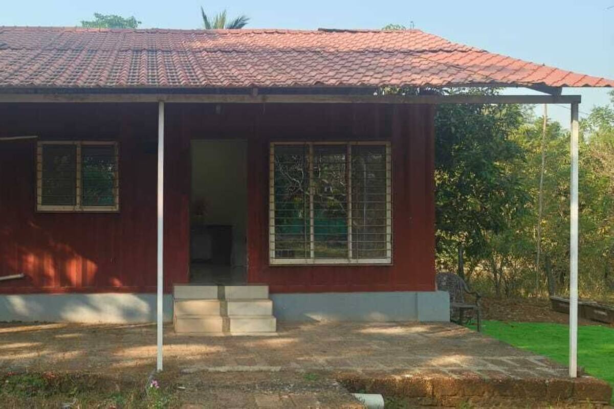 A red house with a tiled roof, two windows with shutters, a porch, and a small front yard.
