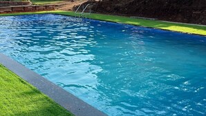 A rectangular swimming pool with clear blue water, surrounded by a grassy area and a stone wall.