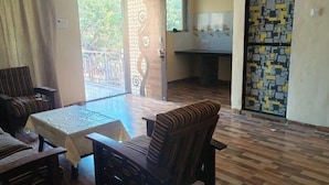 A room with a wooden floor, a dining table with chairs, a sofa, and a view through a door to an outdoor area.