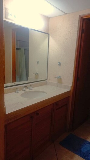 A bathroom with a white sink, wooden cabinets, a mirror, and a blue rug on the floor.