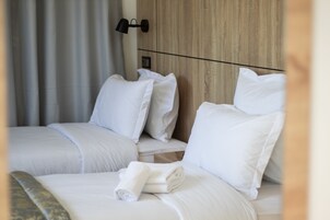 Habitación de hotel con dos camas, ropa de cama blanca, cabecero de madera y una lámpara de pared.