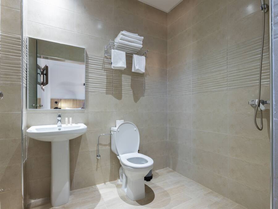 Un baño moderno con lavamanos, inodoro y ducha blancos. Hay un perchero sobre el inodoro y un espejo sobre el lavamanos.
