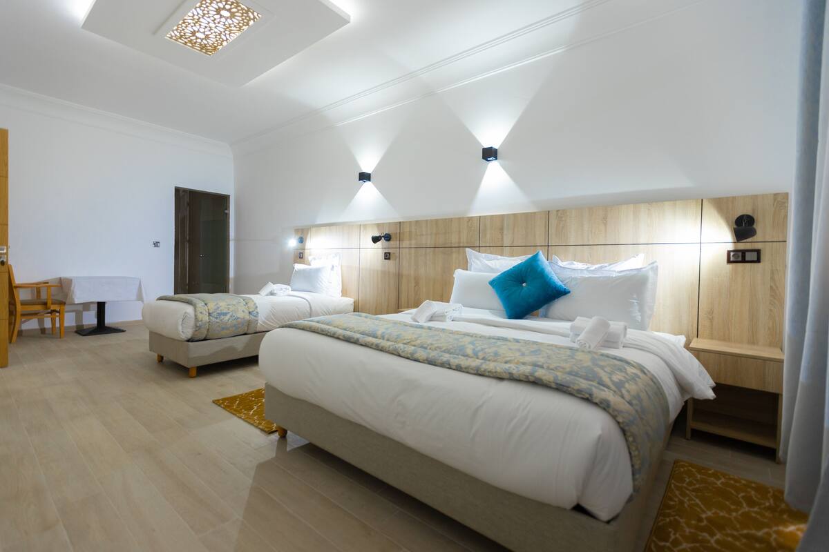 A modern hotel room with two beds, a wooden headboard, and a small desk with a chair.