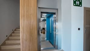 Ein modernes Interieur mit einer Holzsäule, einem blauen Aufzug und einem grünen Notausgangsschild.